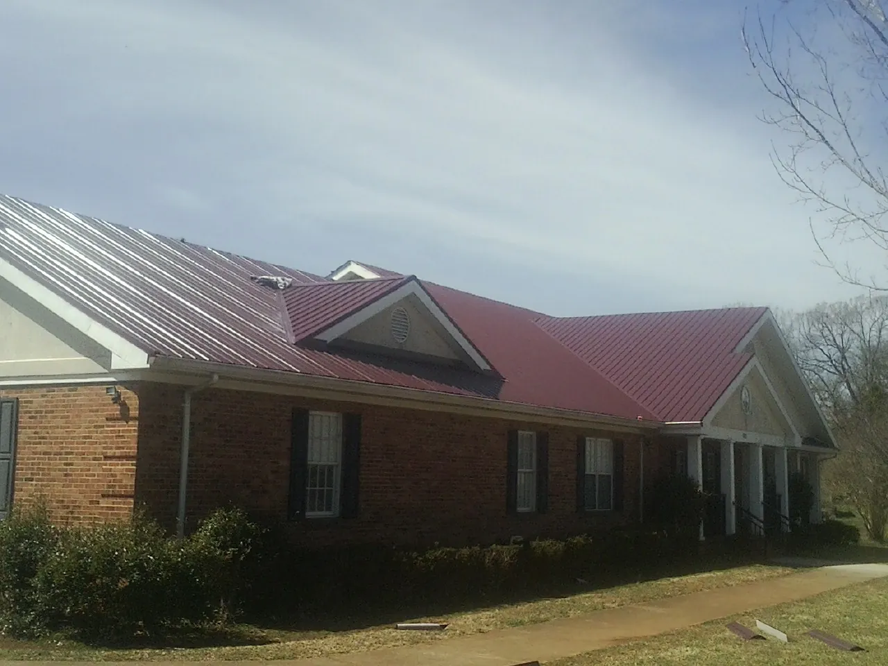 Red metal roof with gabled entries on a long brick building, from a Hail Damage Roof Repair job in Gridley