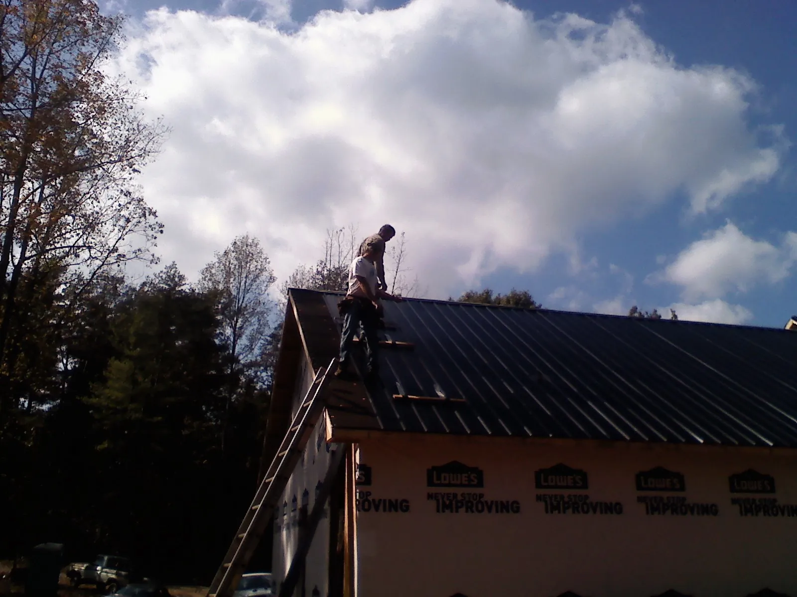 Roofer fastening dark metal panels high against a cloudy sky, from a Roof Inspection job in Gridley
