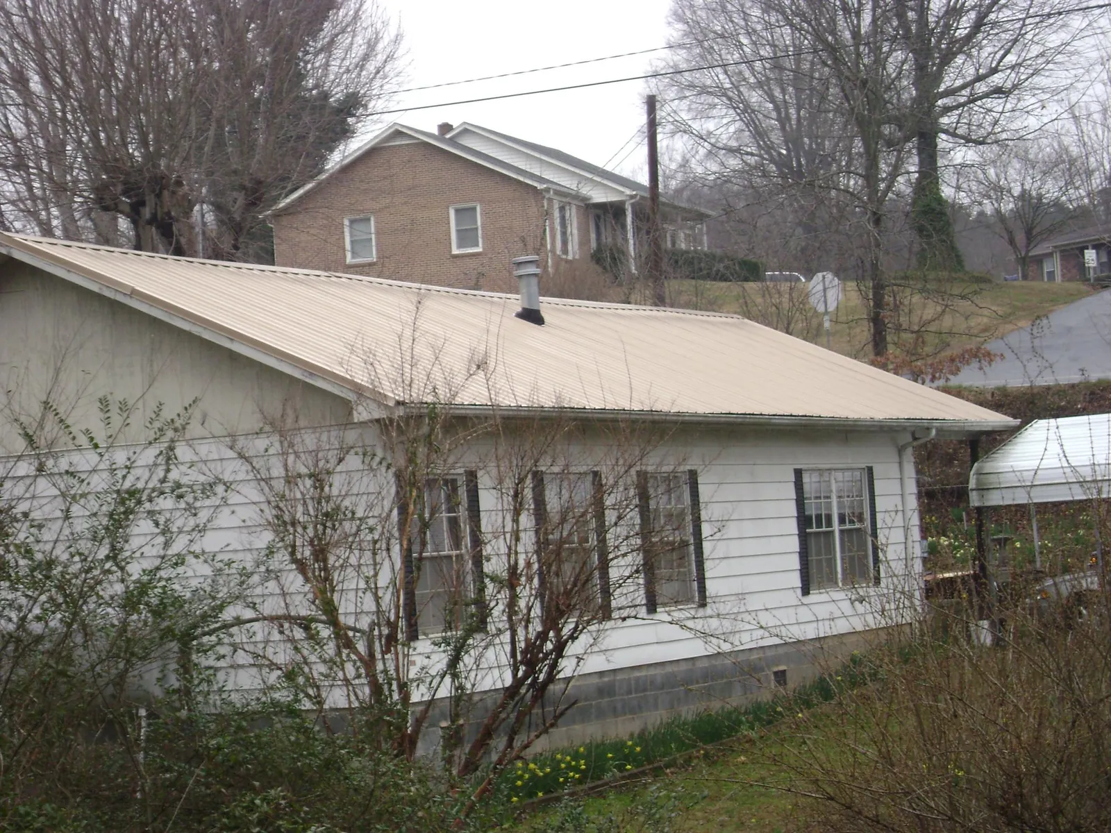 Tan metal roof on a white sided house set into a hillside — Commercial Roofing by Roofing Brothers in Gridley
